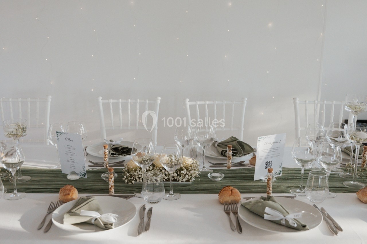 Table élégamment dressée avec nappes blanches, couverts, verres, serviettes pliées et décorations florales.