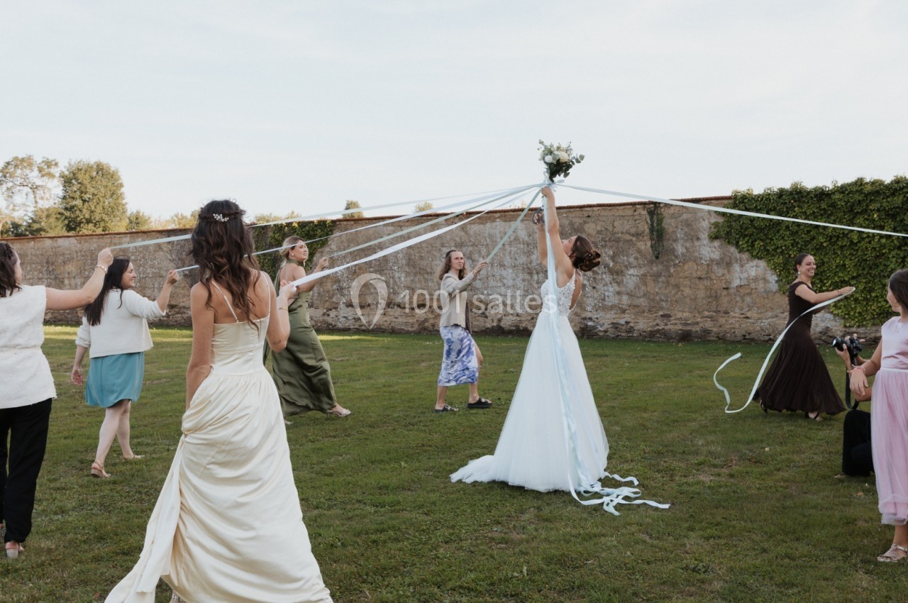 Des femmes dansent en cercle autour d'une mariée tenant des rubans blancs, dans un jardin en plein air.