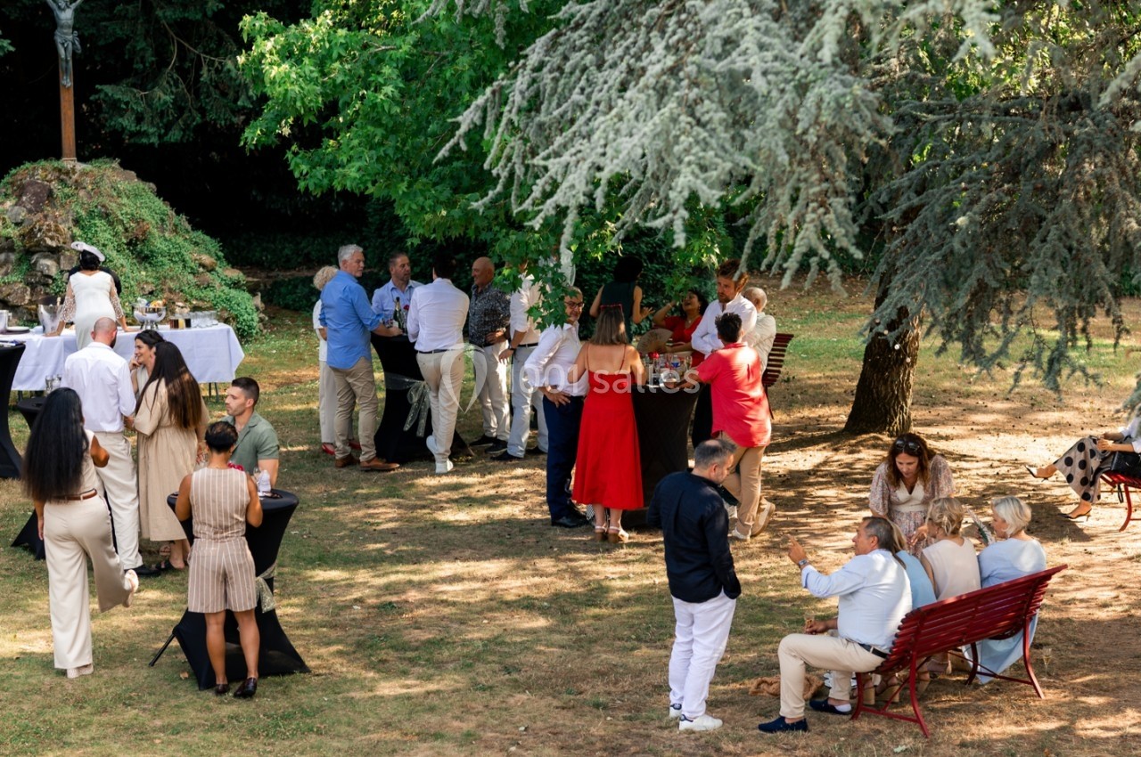 Groupe de personnes discutant et partageant un moment convivial dans un jardin ombragé avec tables et bancs.