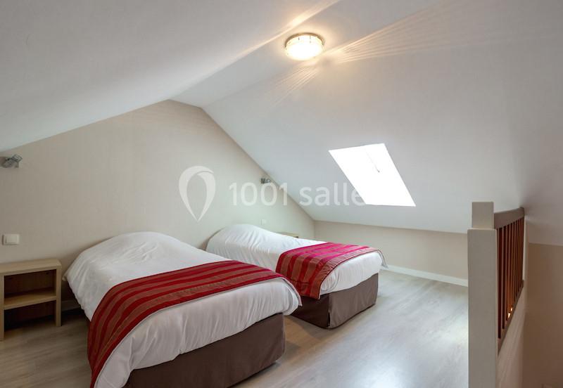Deux lits simples avec couvre-lits rouges dans une chambre mansardée lumineuse avec un plafond incliné et une fenêtre de…