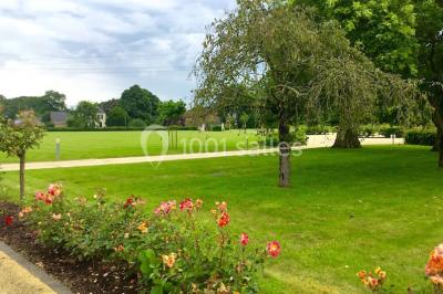Chambre lumineuse avec lit, canapé, télévision murale, bureau et grande fenêtre avec rideaux rouges.