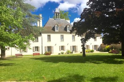 Chambre lumineuse avec lit, canapé, télévision murale, bureau et grande fenêtre avec rideaux rouges.