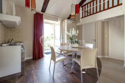 Chambre lumineuse avec lit, canapé, télévision murale, bureau et grande fenêtre avec rideaux rouges.