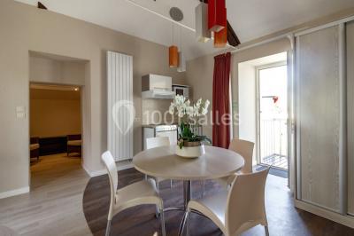 Chambre lumineuse avec lit, canapé, télévision murale, bureau et grande fenêtre avec rideaux rouges.