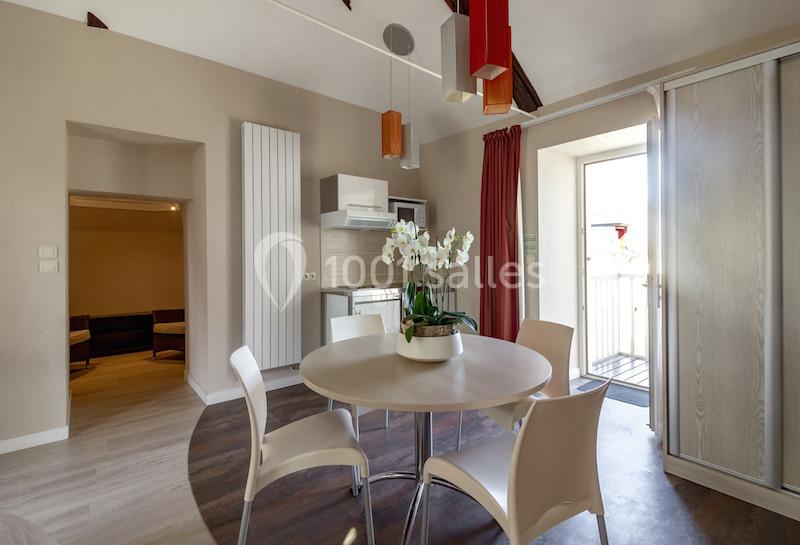 Salle à manger lumineuse avec table ronde, chaises blanches, orchidée en centre de table et accès à un balcon.