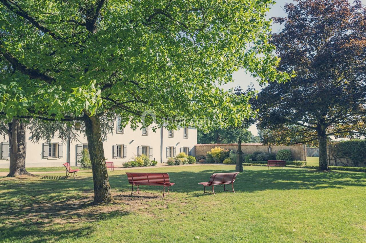 Jardin verdoyant avec bancs rouges, arbres ombragés et bâtiment blanc en arrière-plan par une journée ensoleillée.