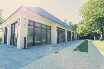 Chambre lumineuse avec lit, canapé, télévision murale, bureau et grande fenêtre avec rideaux rouges.