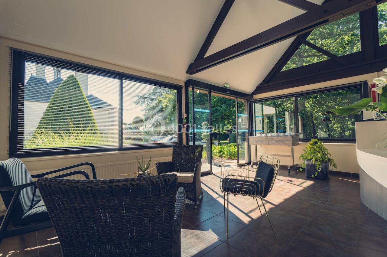 Salle lumineuse avec de grandes baies vitrées, des fauteuils en rotin et vue sur un jardin verdoyant.