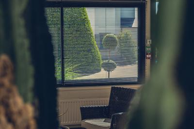 Chambre lumineuse avec lit, canapé, télévision murale, bureau et grande fenêtre avec rideaux rouges.