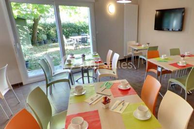 Chambre lumineuse avec lit, canapé, télévision murale, bureau et grande fenêtre avec rideaux rouges.