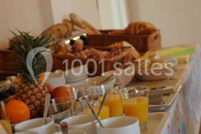 Chambre lumineuse avec lit, canapé, télévision murale, bureau et grande fenêtre avec rideaux rouges.