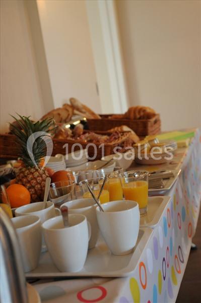 Buffet de petit-déjeuner avec fruits, jus d'orange, viennoiseries et pains disposés sur une table colorée.