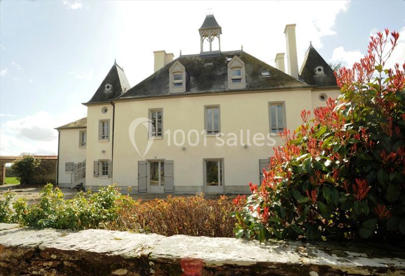 Façade d'un bâtiment ancien avec toit en ardoise, tourelles et jardin arboré au premier plan.