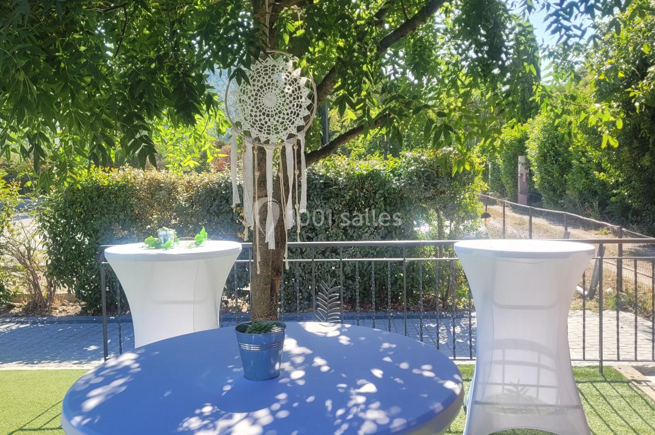 Table haute habillée de blanc sous un arbre, décorée d'un attrape-rêves et entourée de verdure en extérieur.