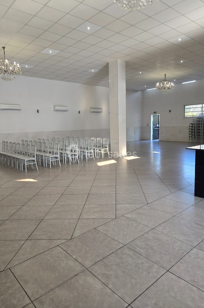 Salle spacieuse avec carrelage clair, chaises alignées sur le côté, lustres suspendus et lumière naturelle.