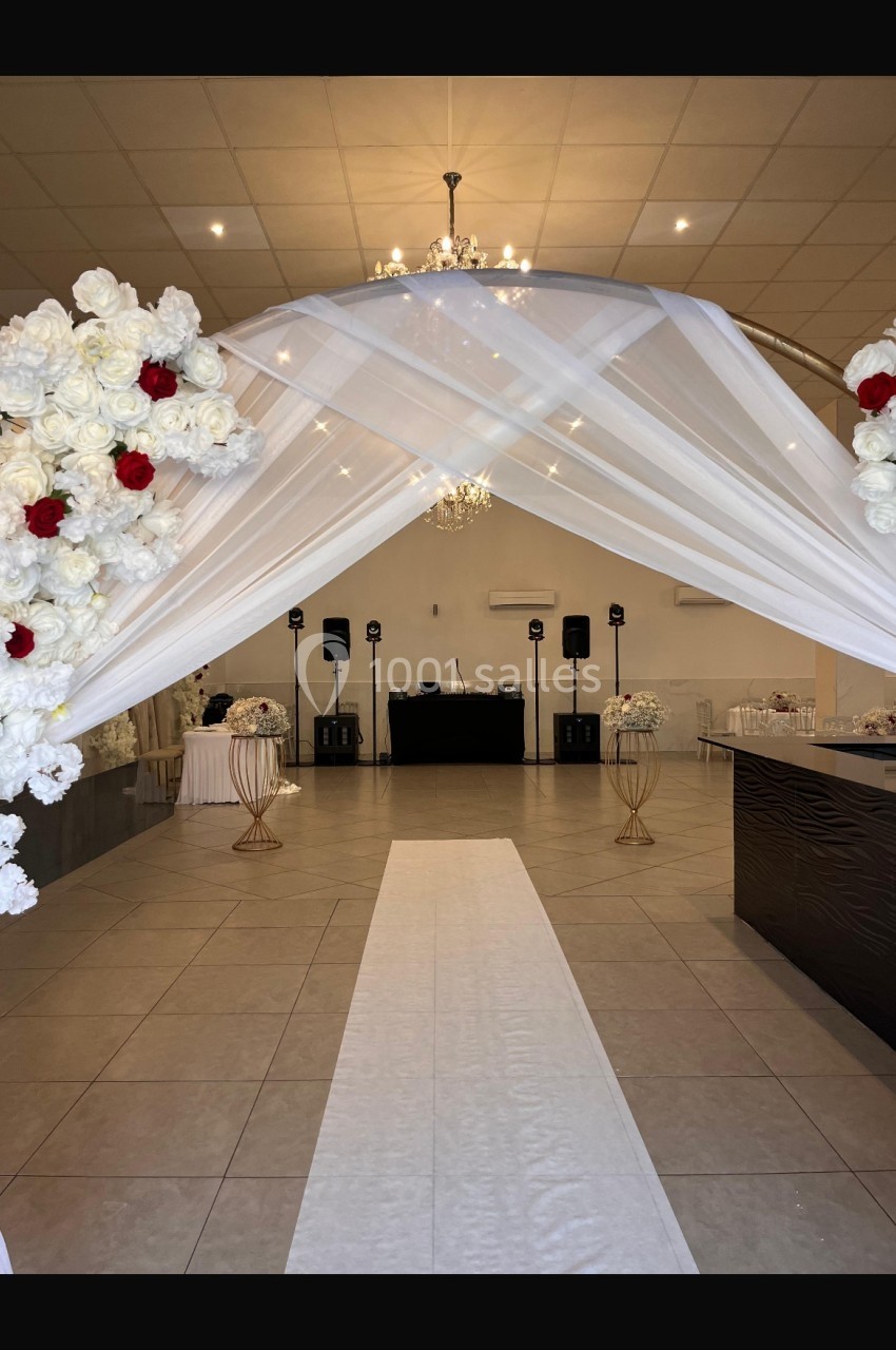 Allée centrale décorée de fleurs blanches et rouges, menant à une scène avec des équipements audio dans une salle de…