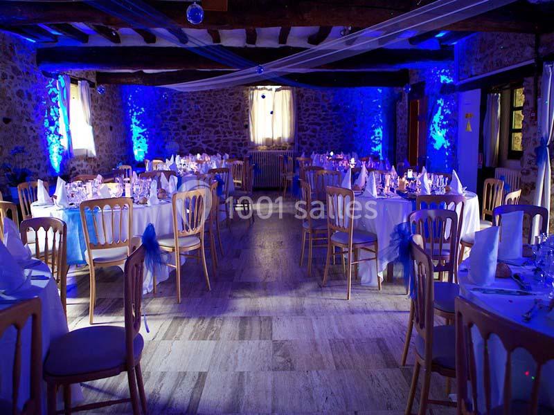 Salle de réception en pierre avec tables dressées et éclairage bleu tamisé.