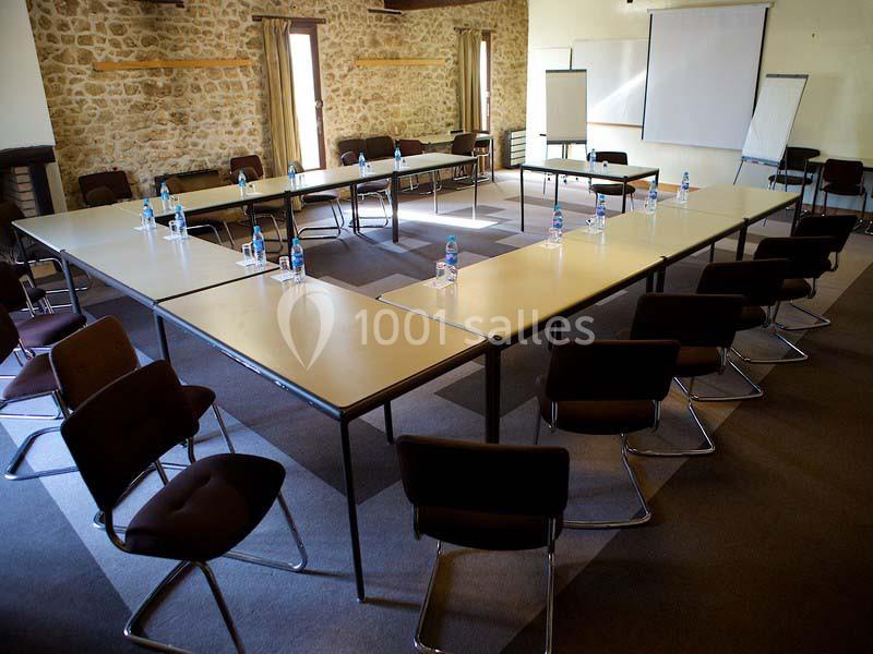 Salle de réunion avec tables disposées en U, chaises, bouteilles d'eau et tableaux de présentation.