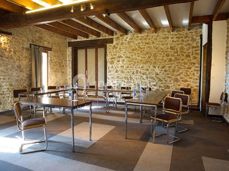 Salle de réunion avec murs en pierre, tables disposées en U, chaises modernes et bouteilles d'eau sur les tables.