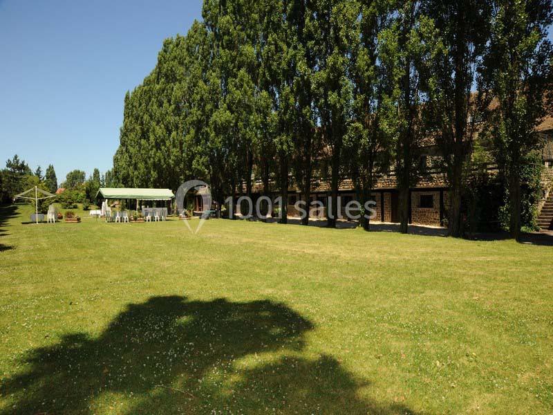 Grande pelouse bordée d'arbres avec une structure couverte et des chaises disposées en extérieur.