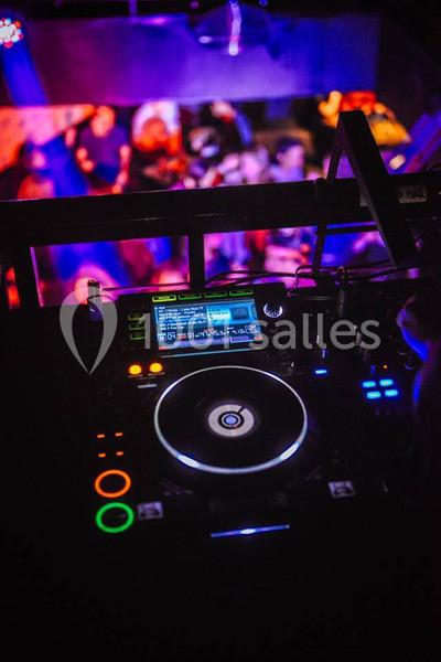 Vue rapprochée d'une table de mixage DJ éclairée, avec une foule floue dansante en arrière-plan.