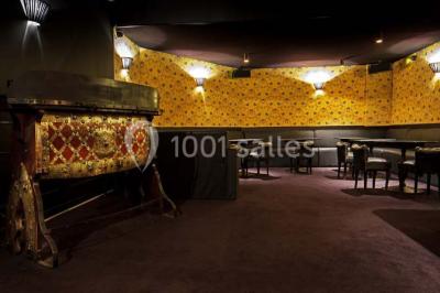 Personne en costume buvant un verre dans un bar faiblement éclairé, avec des lumières floues en arrière-plan.