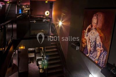 Personne en costume buvant un verre dans un bar faiblement éclairé, avec des lumières floues en arrière-plan.