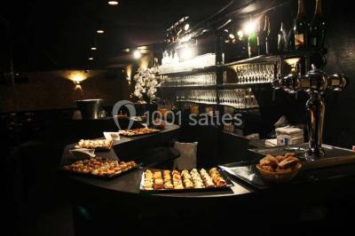 Personne en costume buvant un verre dans un bar faiblement éclairé, avec des lumières floues en arrière-plan.