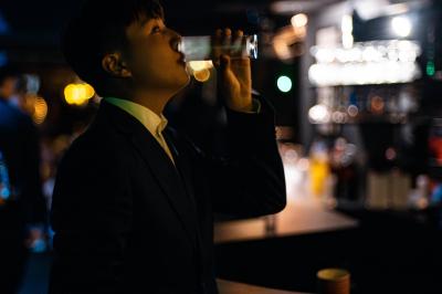 Personne en costume buvant un verre dans un bar faiblement éclairé, avec des lumières floues en arrière-plan.
