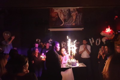 Miniature Location salle Paris 6 (Paris) - Le Scarlett #3 Portrait éclairé d'une femme en tenue d'époque, suspendu au-dessus d'une table ronde avec une lampe verte allumée.
