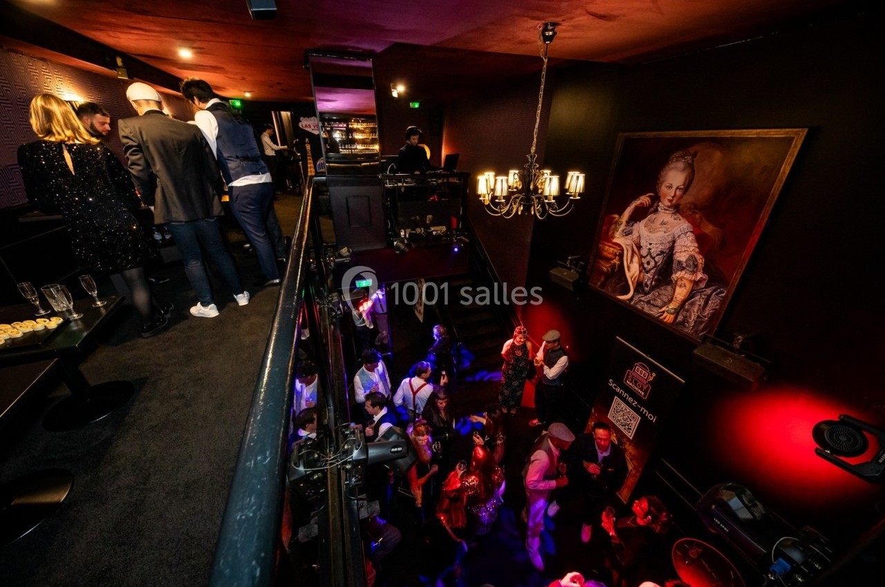 Vue d'une soirée dans un lieu élégant avec des invités debout et dansant, éclairage tamisé et décor raffiné.