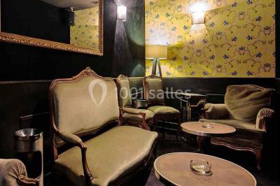 Personne en costume buvant un verre dans un bar faiblement éclairé, avec des lumières floues en arrière-plan.