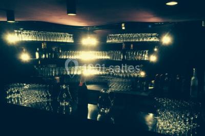 Étagères remplies de verres illuminés par des lumières tamisées dans un bar à l'ambiance sombre.