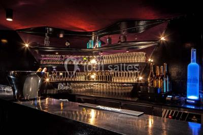 Étagères remplies de verres illuminés par des lumières tamisées dans un bar à l'ambiance sombre.