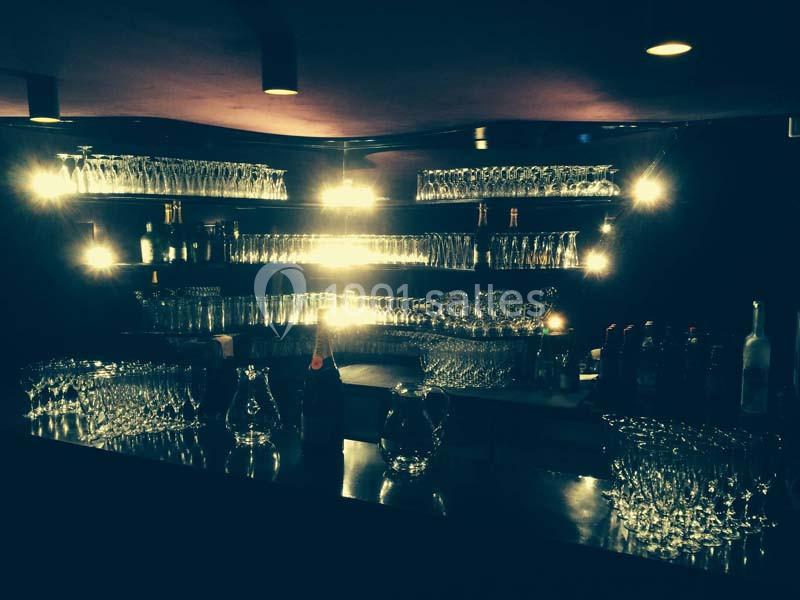 Étagères remplies de verres illuminés par des lumières tamisées dans un bar à l'ambiance sombre.