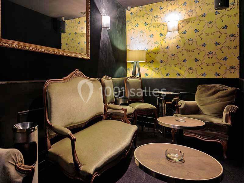 Salon cosy avec fauteuils et canapés anciens, tables basses rondes et mur tapissé de motifs floraux jaunes.