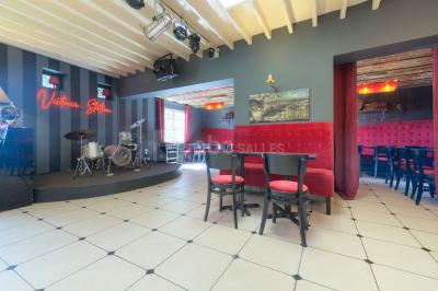 Salle décorée pour un événement avec longues tables dressées, nappes blanches, nœuds roses et portraits accrochés au mur.