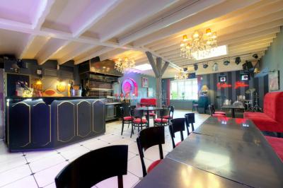 Salle décorée pour un événement avec longues tables dressées, nappes blanches, nœuds roses et portraits accrochés au mur.