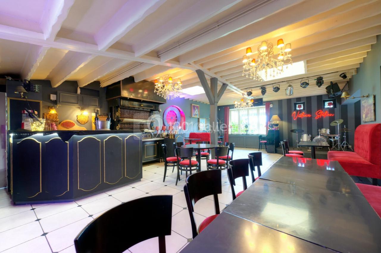 Salle lumineuse avec bar, tables et chaises noires, décorations colorées et lustres suspendus au plafond.