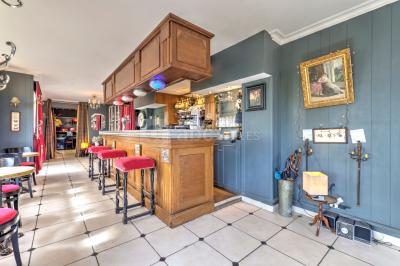 Salle décorée pour un événement avec longues tables dressées, nappes blanches, nœuds roses et portraits accrochés au mur.