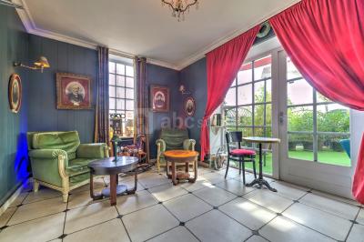 Salle décorée pour un événement avec longues tables dressées, nappes blanches, nœuds roses et portraits accrochés au mur.