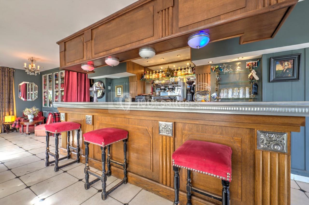 Comptoir de bar en bois avec tabourets rouges, étagères garnies de bouteilles et décoration intérieure lumineuse.