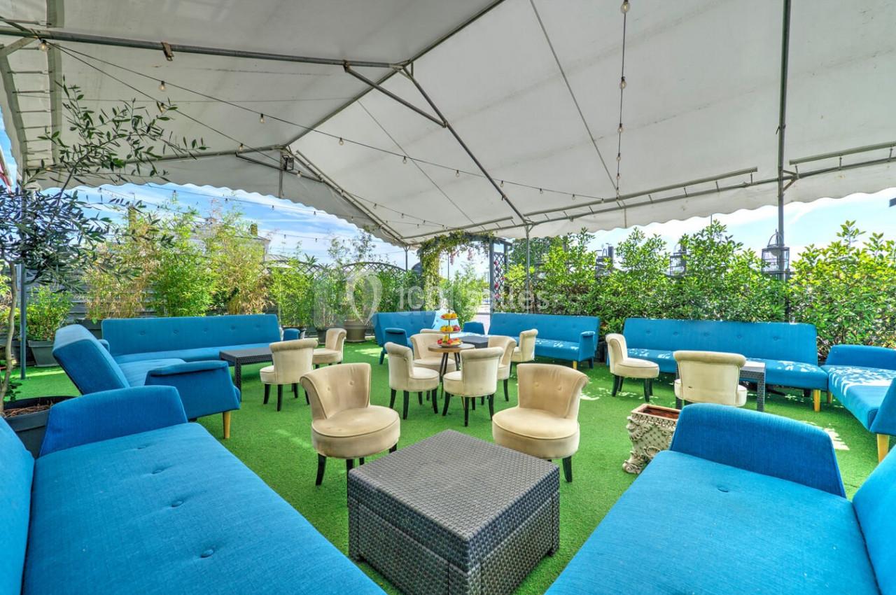 Espace extérieur aménagé sous une tente avec des canapés bleus, des fauteuils beiges et une table basse sur gazon.