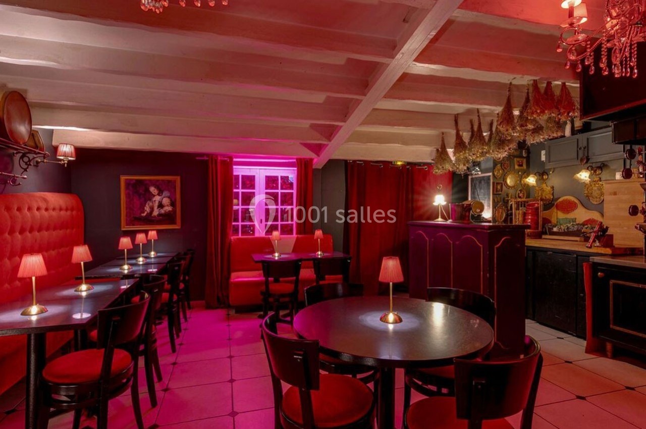Salle de restaurant à l'éclairage tamisé rose, avec tables rondes, chaises noires et décorations murales.