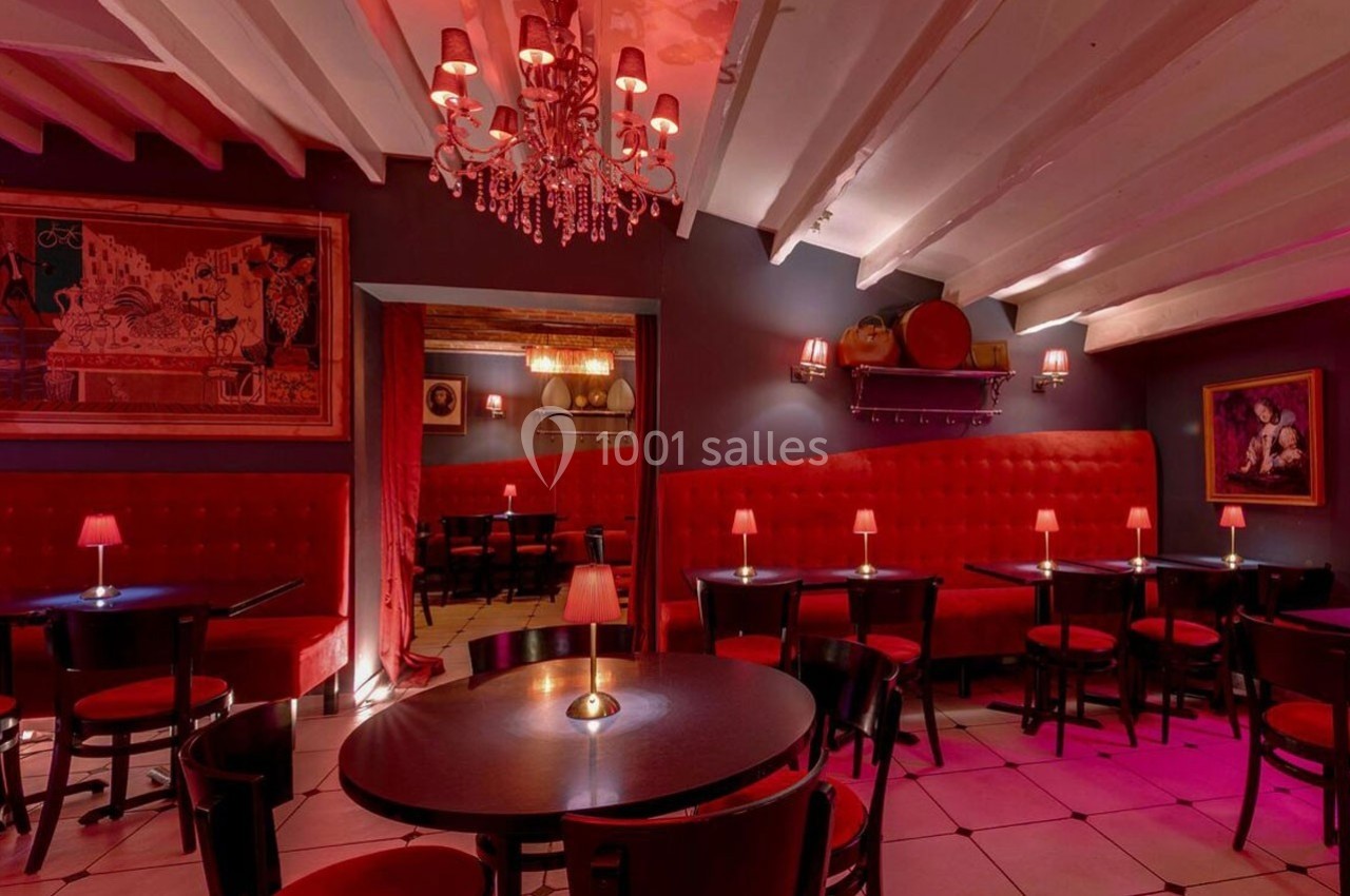 Salle de restaurant avec banquettes rouges, tables rondes, éclairage tamisé et décorations murales.