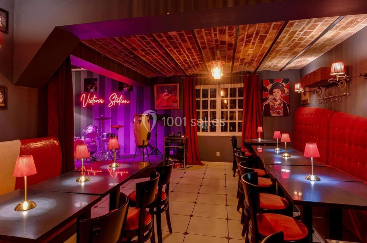 Salle de restaurant avec tables, chaises, éclairage tamisé et une scène équipée d'instruments de musique.