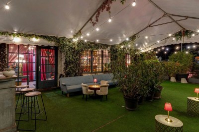Terrasse extérieure avec tables et chaises en bois sous des auvents, entourée de verdure et de ciel dégagé.