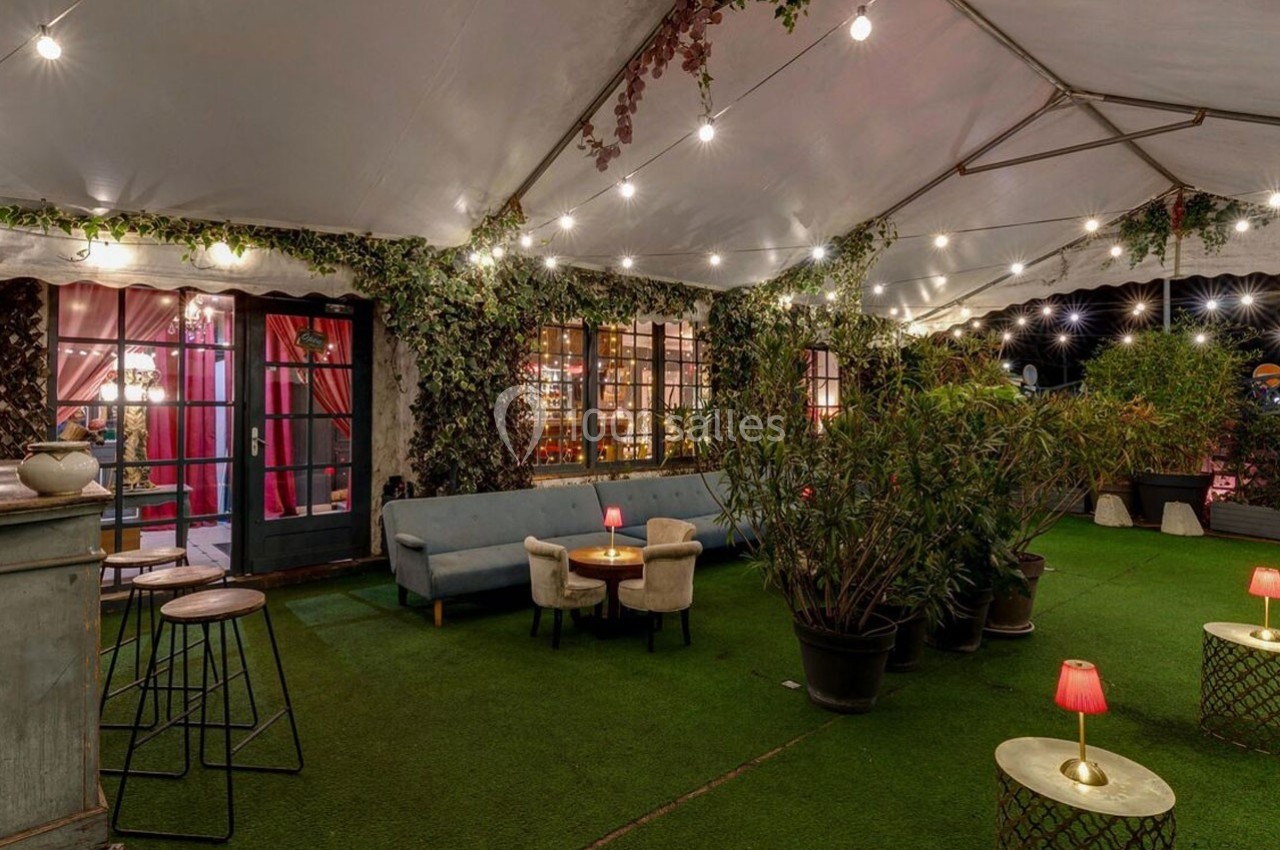 Espace extérieur couvert avec éclairage chaleureux, mobilier confortable, plantes et ambiance conviviale.