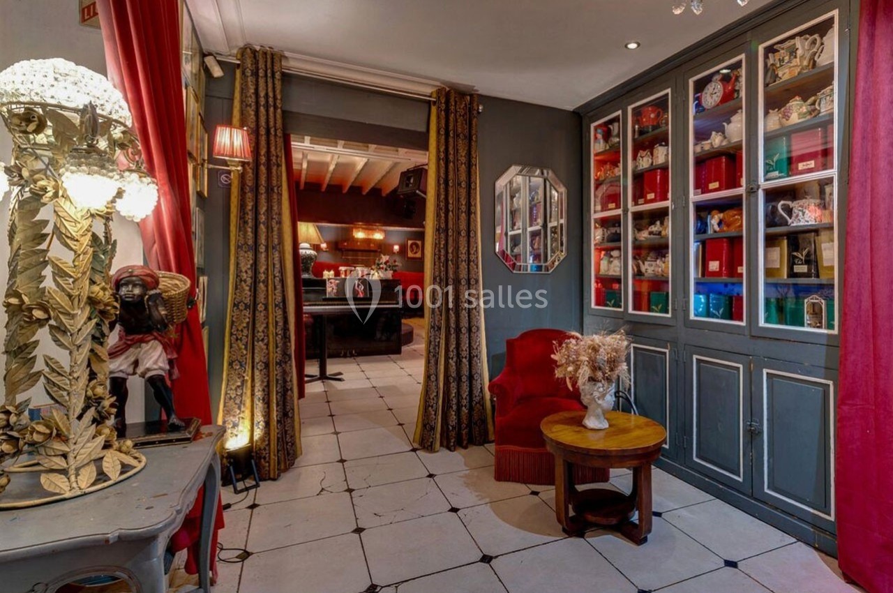Intérieur d'une pièce décorée de meubles anciens, vitrines remplies d'objets, rideaux dorés et fauteuil rouge.