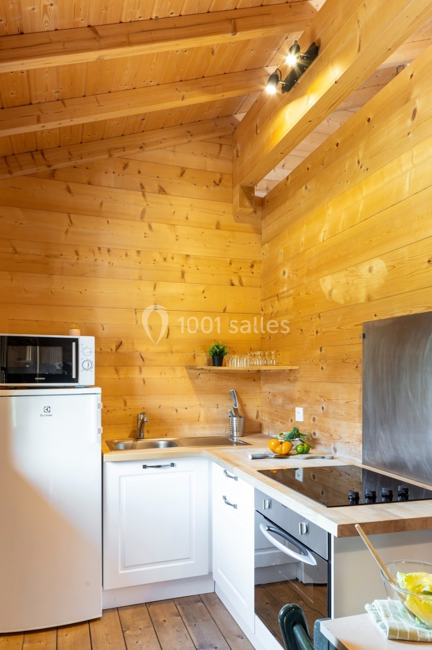 Cuisine en bois clair avec un plafond en poutres apparentes, équipée d'un réfrigérateur, d'un four et d'une plaque de…